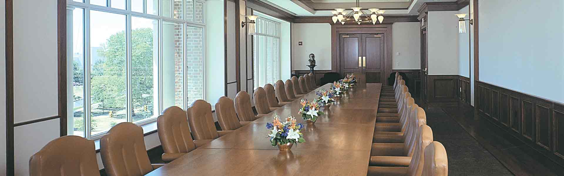 Board Room with long table with chairs. Bordered on left with windows.