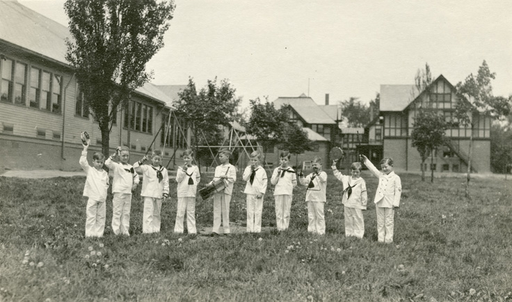 Boys dressed in sailor suits holding instruments outside.