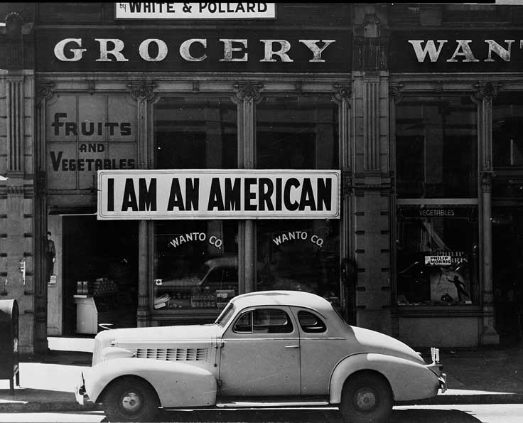1940s car parked in front of grocery with a sign that reads I AM AN AMERICAN.