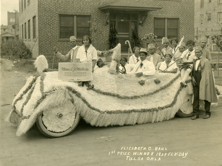 Men and women in a car decorated for a parade.