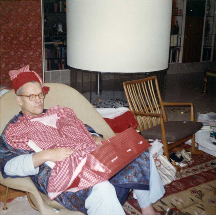 Man in chair with gift-wrapping and new pajamas laid over him. 
